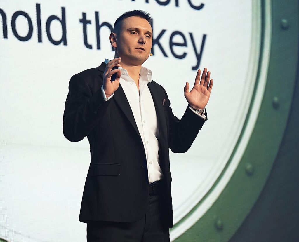 A real photograph of Maksym Sakharov in a suit during a conference