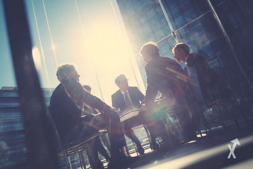 Five men discussing in glass building, resembling FOMC meeting.